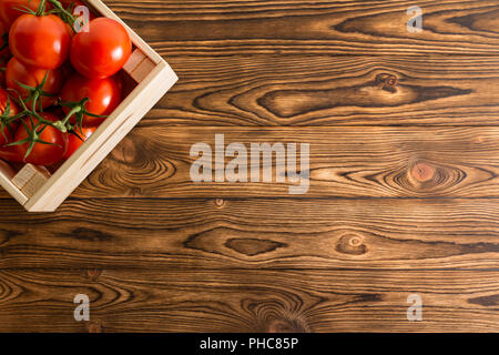 Fruits rouges juteux les tomates biologiques dans une caisse en bois placé dans le coin d'une table en bois rustique au marché de fermiers avec copie espace Vue de dessus Banque D'Images