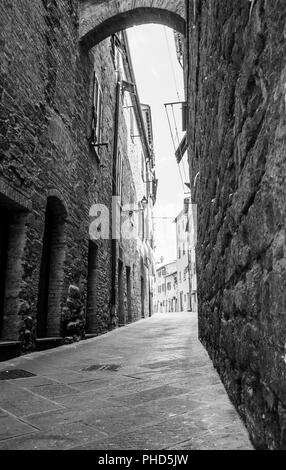 Les murs de pierre brute en étroite ruelle sombre bordée de hauts édifices de pierre menant à venir. rue lumineux Banque D'Images