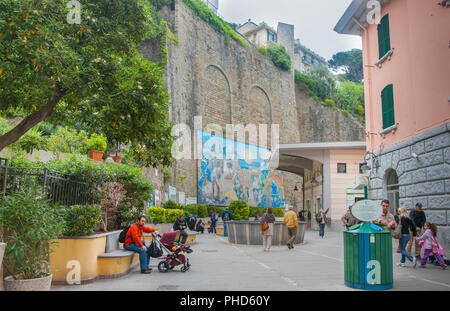 RIOMAGGIORE ITALIE - Le 24 avril 2011 ; les gens de passage ou d'attente en place près de la gare ferroviaire de côtières avec l'art murale sur mur de briques. Banque D'Images