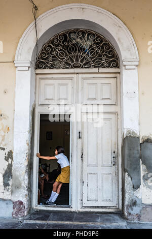 Cienfuegos, Cuba / 15 mars 2016 : Girl in school uniform debout à ouvrir la porte d'entrée voûtée hauteur usés. Banque D'Images