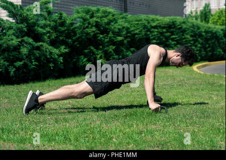 Jeune athlète man doing push up avec push-up bars sur le plancher, le sport et la formation dans les concepts d'herbe Banque D'Images