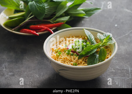 Dans un bol de nouilles instantanées à l'aide de fines herbes, garnir de coriandre et basilic Asiatique, citron, citron vert foncé sur fond de pierre Banque D'Images