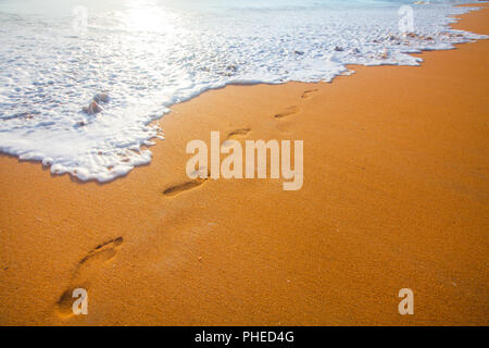 Plage, vague et empreintes de pas à l'heure du coucher du soleil Banque D'Images