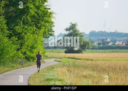 L'exécution de femme vu de dos sur une route pavée à travers prés et arbres à côté du Parc National Neusiedlersee en Burgenland, Autriche. Banque D'Images