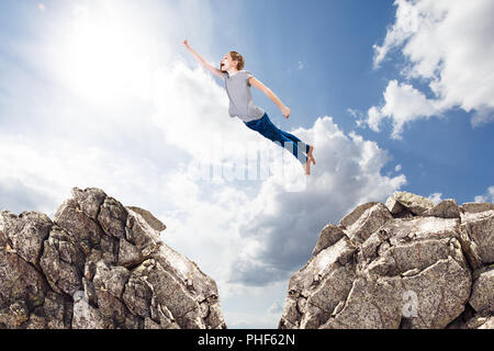 Petite fille mignonne comme un vol de supergirl à partir d'un rocher à l'autre. Banque D'Images