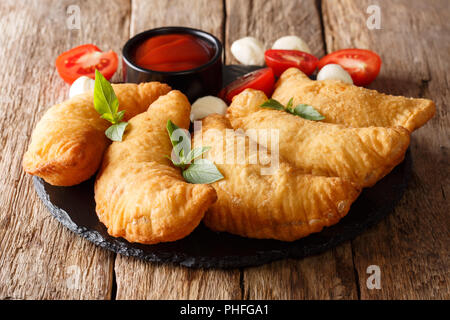 Sex fried panzerotti pizza fraîche du avec un remplissage de tomates, herbes et mozzarella close-up sont servis sur un tableau noir. Banque D'Images