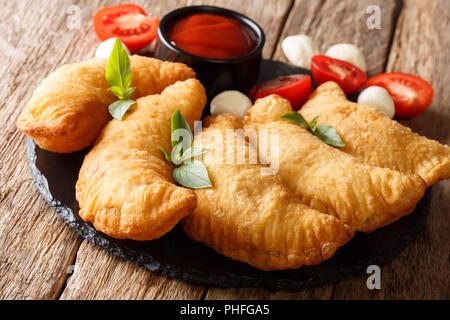 Panzerotti pizza fraîche du frit avec une garniture de tomates, herbes et mozzarella close-up sur un tableau noir. Banque D'Images