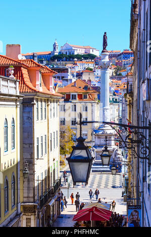 Lisbonne, Portugal - 27 mars 2018 : vue panoramique de rue menant à la place Rossio, rangée de lanternes, statue et maisons sur la colline Banque D'Images