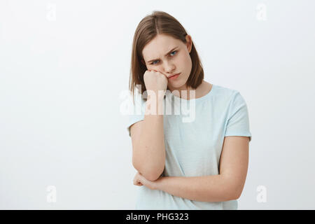 Studio shot of déplut offensé et lugubre mignon femelle brune en t-shirt se penchant sur le visage et lèvres sourcils poing à la recherche de sensation de l'envie ou jaloux en voyant une sœur a reçu super cadeau de parents Banque D'Images