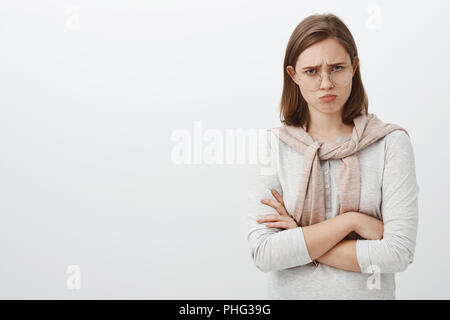 Taille plan sur triste malheureux et lugubre fille mignonne avec l'oreille de froncer et battit bouder crossing arms plus de corps sentir jaloux ou de regret d'être puni par les parents mécontents permanent sur mur gris Banque D'Images