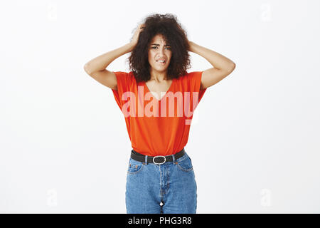 Tourné à l'intérieur de l'anxieux Troubles de peau foncée femme avec coupe afro de mordre la lèvre, se tenant la main sur la tête et avoir de gros problèmes, l'article sur fond gris, nerveux, s'inquiétant de la vie Banque D'Images