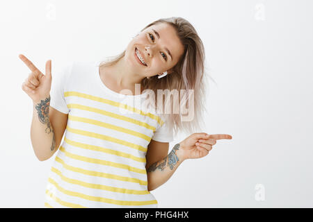 Girl enjoying moment avec la grande musique dans des écouteurs. Bien positive et heureuse femme, danse et tilting head de côté en pointant dans différentes parties, écouter des chansons dans des écouteurs sans fil Banque D'Images