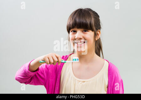 Little girl holding toothbrush sur fond gris. Banque D'Images