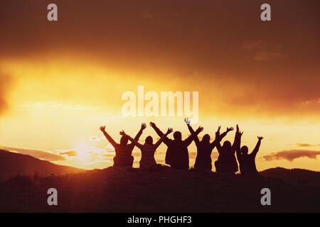 Happy friends avec bras levés silhouettes au coucher du soleil Banque D'Images