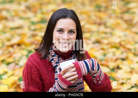 Jeune femme souriante avec tasse de thé dans un parc d'automne Banque D'Images