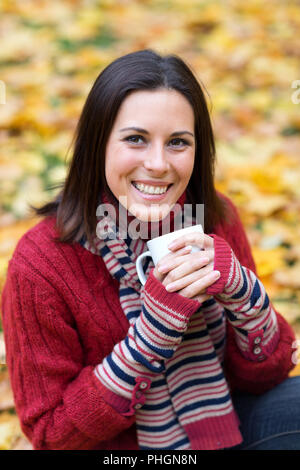 Jeune femme souriante avec tasse de thé dans un parc d'automne Banque D'Images