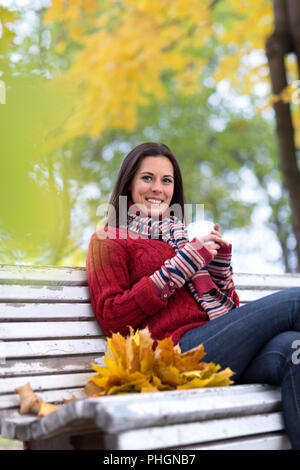 Jeune femme souriante avec tasse de thé dans un parc d'automne Banque D'Images