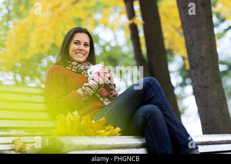 Jeune femme souriante avec tasse de thé dans un parc d'automne Banque D'Images