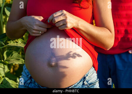 Fille enceinte dans la nature. Séance photo d'une fille enceinte à jint et rouge t-shirt dans un champ au coucher du soleil Banque D'Images