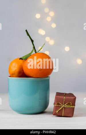 Mandarines biologiques dans une tasse en céramique bleu, et petit cadeau sur fond blanc avec bokeh Banque D'Images