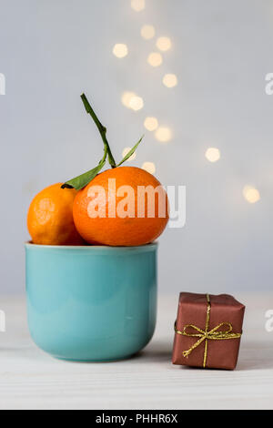 Mandarines biologiques dans une tasse en céramique bleu, et petit cadeau sur fond blanc avec bokeh Banque D'Images