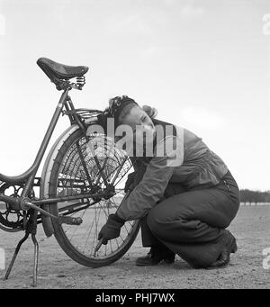 1940 couple avec un vélo. Une jeune femme est pompage d'air dans le pneu arrière de son vélo. Elle porte les vêtements de sport typique des années 40 avec un pantalon long et une veste courte. Filet de protection contre les avis monté sur la roue arrière pour éviter d'étendage de se faire attraper dans la roue. Suède 1942. KristofferssonA Photo89-1 Banque D'Images