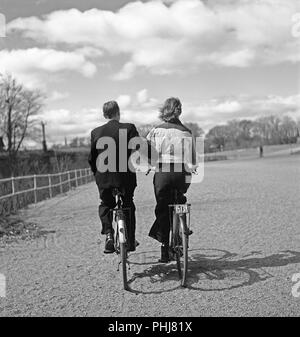 1940 couple sur des bicyclettes. Un jeune couple est équitation leurs bicyclettes sur une journée de printemps ensoleillée. Dans l'amour comme ils le sont, qu'ils soient en possession d'armes même lorsque sur leurs bicyclettes. L'avis d'inscription Inscrivez-vous sur son vélo, comme ce point est obligatoire pour prouver que vous avez payé la taxe location. Suède 1942. Une photo Kristoffersson88-5 Banque D'Images