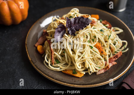 L'automne des pâtes avec du bacon et de la citrouille sur la plaque. Spaghetti maison pâtes potiron avec bacon, fromage parmesan et basilic sur noir, copiez l'espace. Les aliments d'automne Banque D'Images