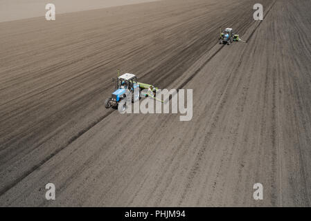 Deux tracteur bleu vif de labourer le sol contre un arrière-plan de la terre noire. Banque D'Images