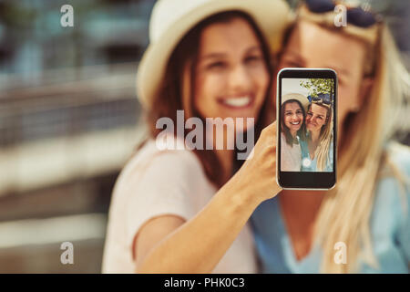 Deux smiling young female friends en tenant vos autoportraits avec un cellulaire tout en profitant d'une journée passée ensemble dans l'été Banque D'Images