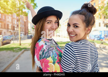 Portrait of smiling young deux amies debout dans les bras tout en marchant à travers la ville sur une journée ensoleillée Banque D'Images