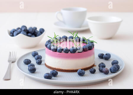 Les deux couleurs mini bleuets gâteau au fromage. Sans cuisson ronde cheesecake, bol avec les bleuets, tasse de café et un bol de sucre. Haut de gâteau décoré par Banque D'Images