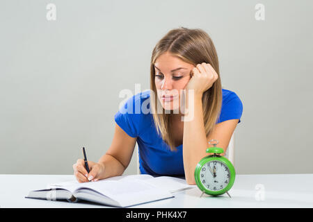 Triste étudiante ne veut pas d'étudier,mais l'horloge est montrant qu'il n'y a pas de beaucoup de temps. Banque D'Images