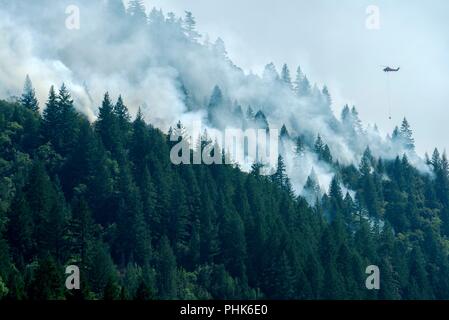 Un hélicoptère transporte un seau bambi avec de l'eau sur les incendies de forêt à la forêt nationale de Mendocino, 16 août 2018 près de saules, en Californie. Le complexe de Mendocino incendie a détruit 157 maisons, tué un pompier et brûlé 459 102 hectares de forêt à devenir la plus grande histoire de la Californie. Banque D'Images