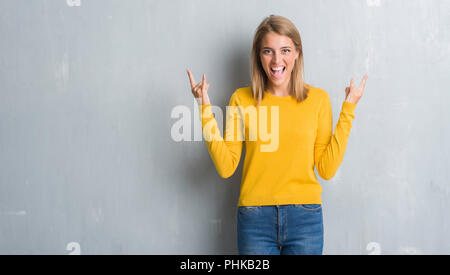 Belle Jeune femme debout sur un mur gris grunge criant avec crazy expression faisant rock symbole avec les mains. Music star. Concept lourd. Banque D'Images