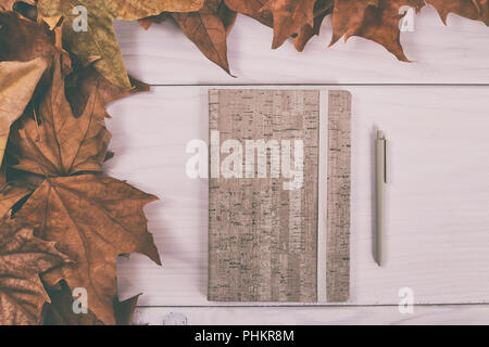 Carnet et un stylo sur la table en bois avec les feuilles d'automne.Image est volontairement tonique. Banque D'Images