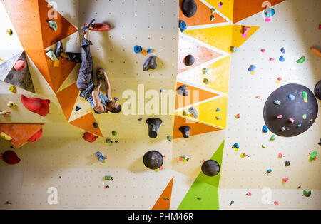 Jeune homme musclé difficile escalade bouldering itinéraire. Dans la salle d'escalade intérieur Banque D'Images
