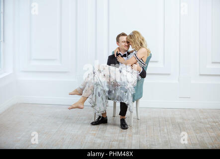 Jeune couple dans le quartier à la mode de vêtements de luxe s'embrasser et de rire tout en restant assis dans un fauteuil à l'intérieur Banque D'Images