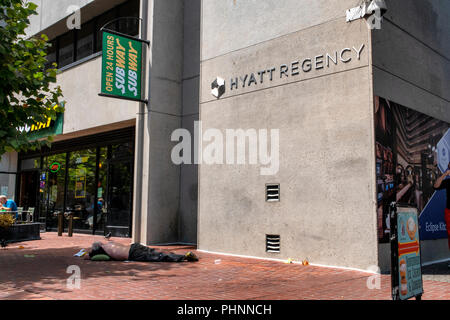 Un sans-abri dort sur la rue devant l'hôtel Hyatt Regency et un métro à San Francisco, Californie. Banque D'Images