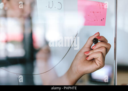Main de l'écriture exécutive féminine sur le mur de verre. femme d'affaires mettant ses idées sur le mur de verre transparent lors d'une réunion. Banque D'Images