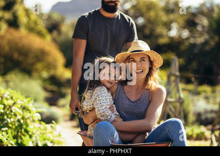 Man pushing woman et petite fille en brouette. Mère et fille ride en brouette poussée par le père dans la ferme. Banque D'Images