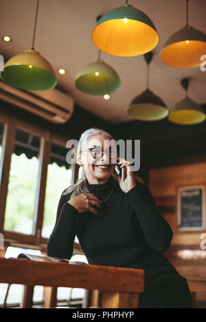 Portrait de senior woman sitting in cafe conversation sur téléphone mobile. Femme mature passez un appel téléphonique au coffee shop. Banque D'Images