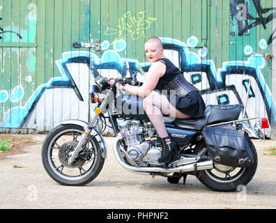 Rosa Fury assis sur une moto Suzuki, ayant fait signe . Elle porte une courte robe noire et collants résille et dispose d'un casque de moto en face d'elle Banque D'Images