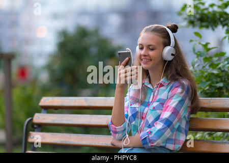 Happy young woman relaxing écouter de la musique sur un banc dans un parc ou jardin sur son téléphone portable avec un sourire heureux et copy space Banque D'Images