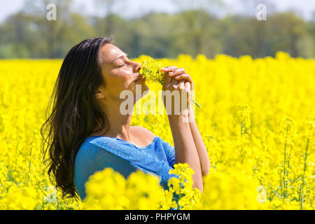 Woman smelling flowers in yellow rapeseed field Banque D'Images