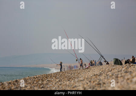 À l'ouest, un pêcheur jette sur plage de Chesil un jour chaud avec une brume de chaleur passant de la plage le 1 septembre 2018 avec beaucoup d'autres pêcheurs à Banque D'Images