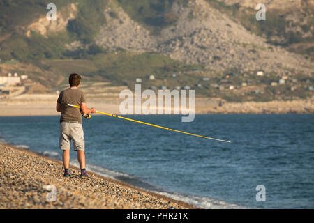 Un pêcheur en fin d'après-midi de pêche du maquereau sur la plage de Chesil sur fond de l'anse de Chesil et les falaises de l'Île de Portland. Dorset Banque D'Images