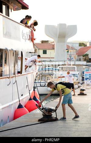 Vodice, Croatie - le 11 août 2018 : un bateau de croisière Carpe Diem arrivant à Vodice et l'amarrage. Un homme et un adolescent sur un quai de fixation de la corde de bateau Banque D'Images