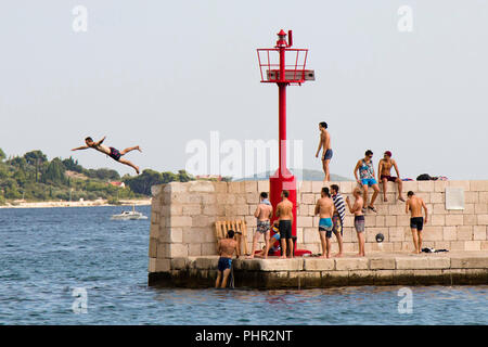 Vodice, Croatie - 2 août 2018 : les jeunes hommes en maillot de bain debout sur la jetée et regarder un homme qui saute dans la mer en été Banque D'Images