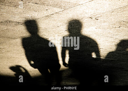 Les ombres des silhouettes d'hommes debout sur la promenade d'été en sépia Noir et blanc Banque D'Images